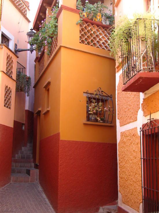 Un estrecho callejón con un edificio pintado en dos colores, una escalera y una reja de metal.