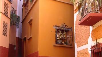 Un estrecho callejón con un edificio pintado en dos colores, una escalera y una reja de metal.