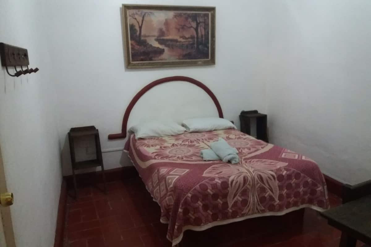 Un dormitorio con cama, un cuadro en la pared, una mesita de noche y una mesita auxiliar.