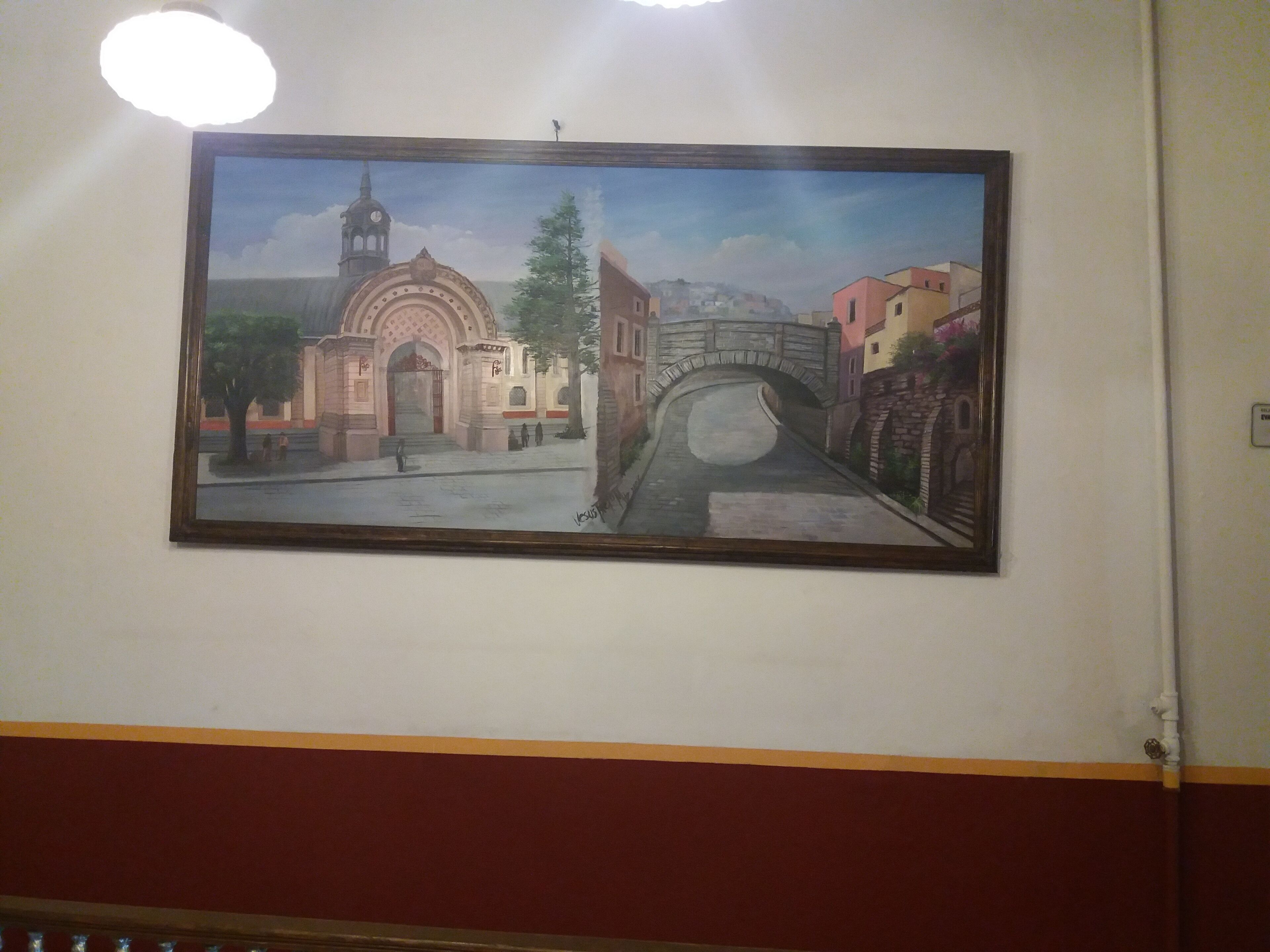 A framed painting of a town square with a prominent building and a bridge.
