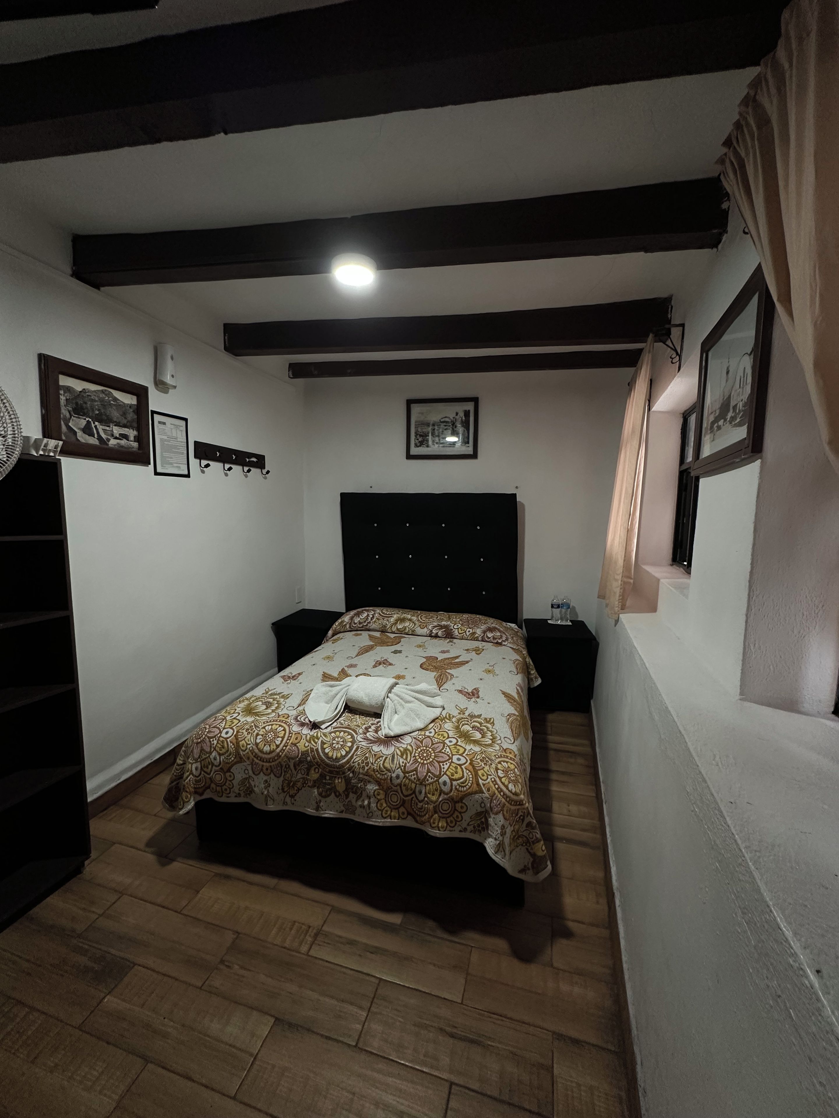 Une chambre à coucher avec un lit, un plancher en bois, un ventilateur de plafond et un luminaire fixé au mur.