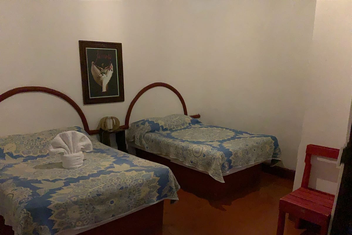 Dos camas con ropa de cama floral, un cuadro en la pared y una silla roja.