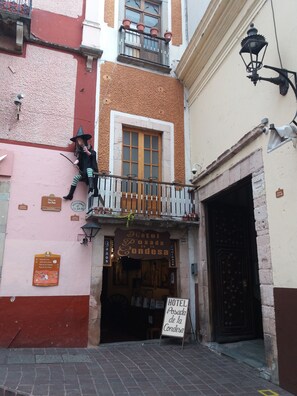 Un edificio con un cartel que indica Hotel Posada de la Cordesa, un balcón con una persona disfrazada y una señal de calle que dice Plaza de la Paz.