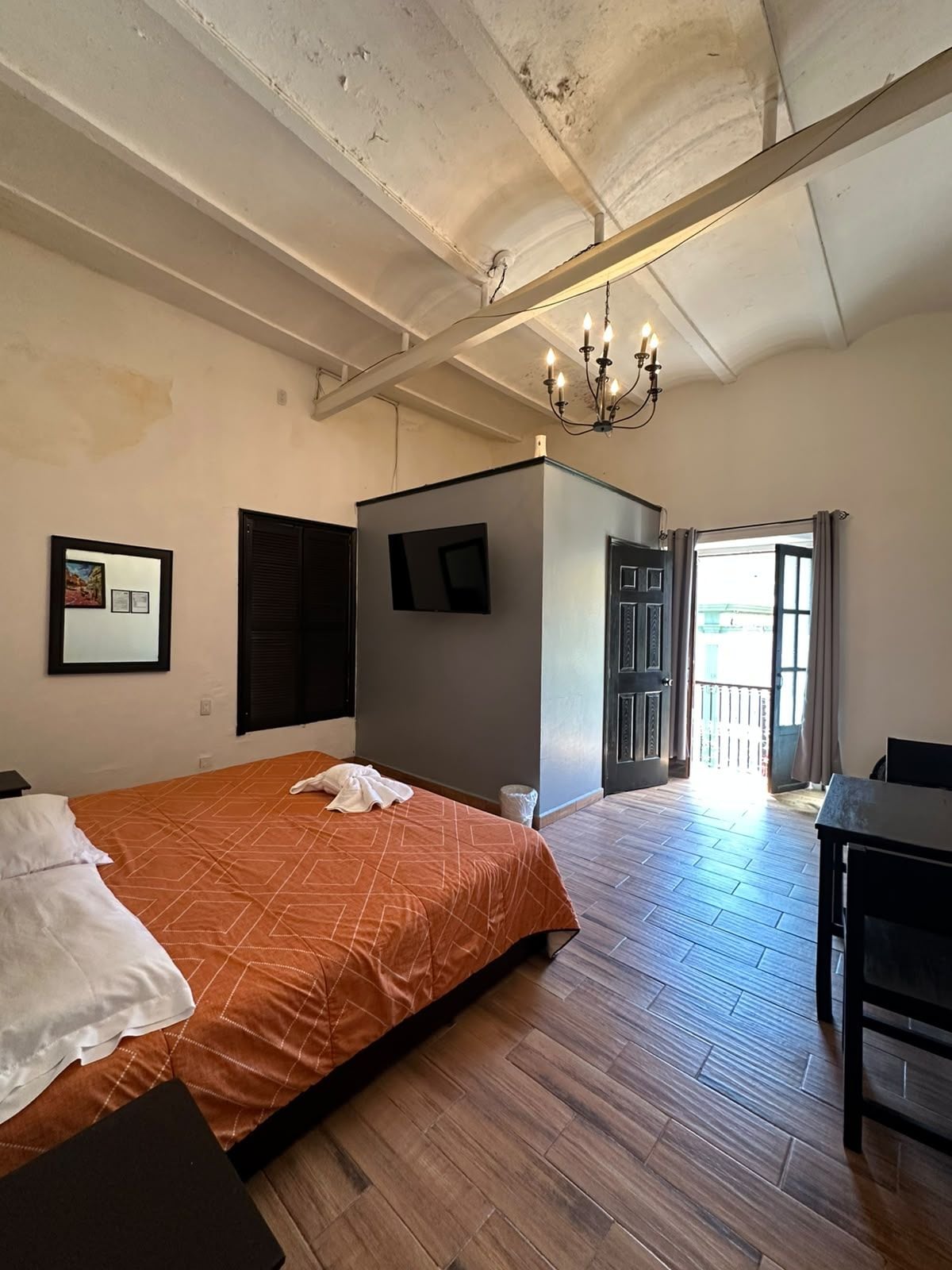 Une chambre d’hôtel avec un lit, un bureau, un téléviseur fixé au mur et un lustre.