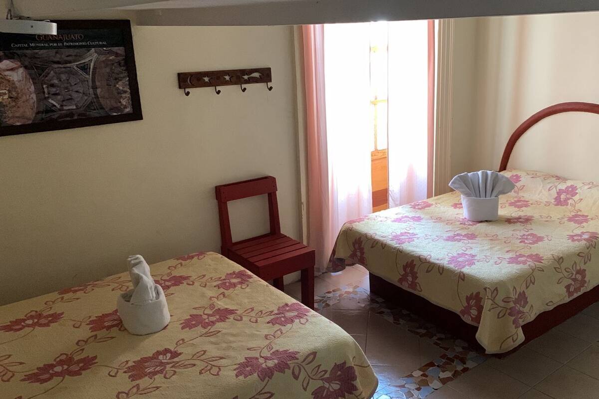 Un dormitorio con dos camas, una silla, una mesita y un estante en la pared.