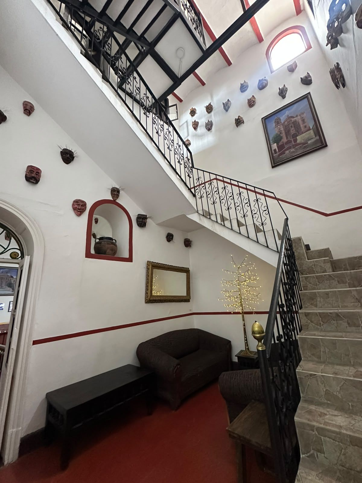 A staircase with a black railing, a red carpeted floor, and various wall decorations including masks and a framed picture.