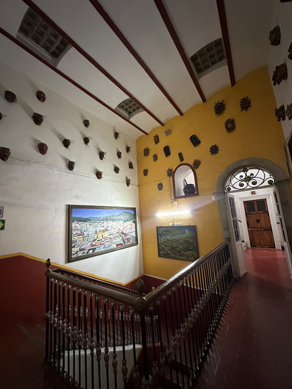 A staircase with ornate balusters, a cityscape painting, and a door with decorative metalwork.