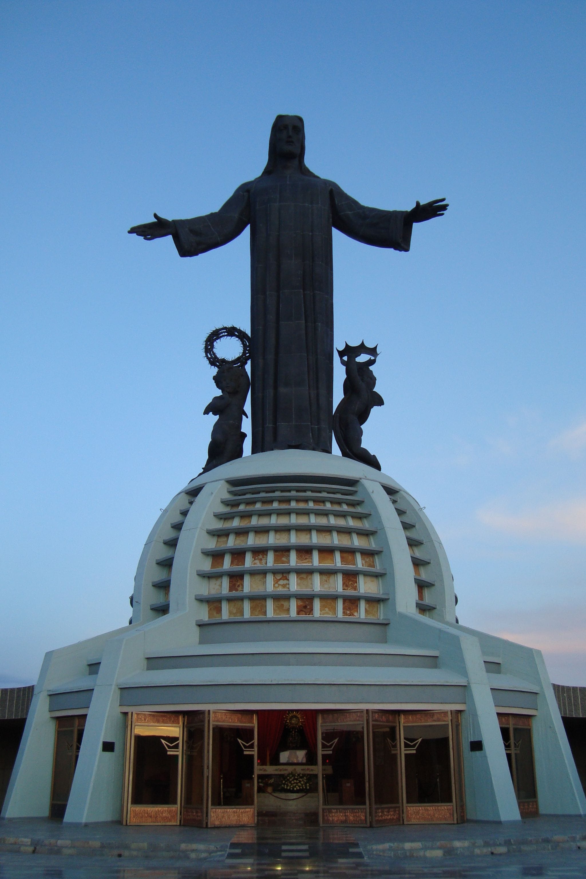 A large statue with outstretched arms on top of a building with a dome and a lower entrance.