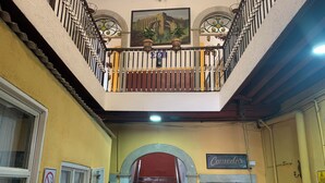 Un couloir avec un escalier rouge, un balcon orné de balustrades décoratives et deux statues dorées.