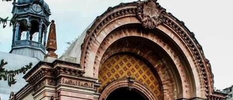 Un edificio histórico con una entrada ornamentada, una torre del reloj y un área vallada con gente.