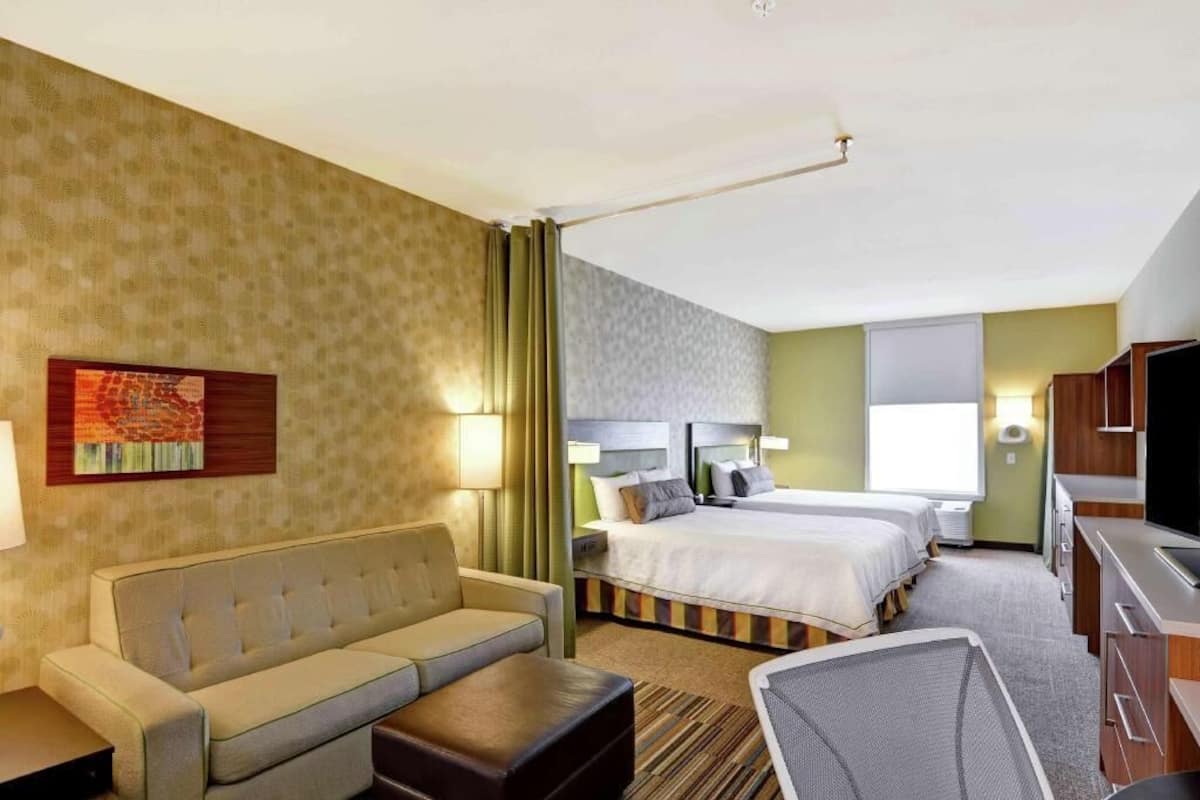 A hotel room with a sofa, two beds, a TV, and a desk.