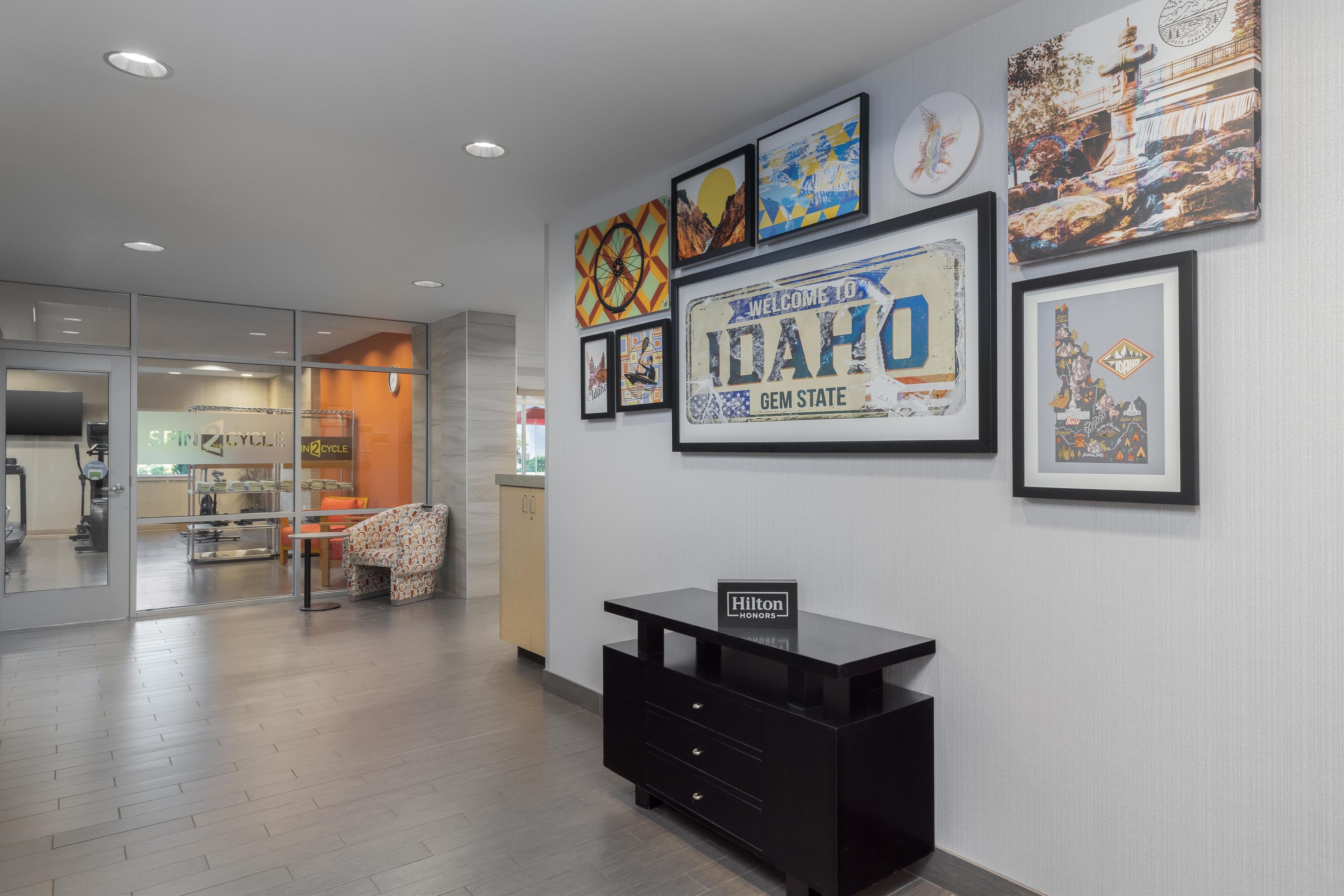 A hotel lobby with a reception desk, framed artwork on the wall, and a glimpse of the dining area in the background.