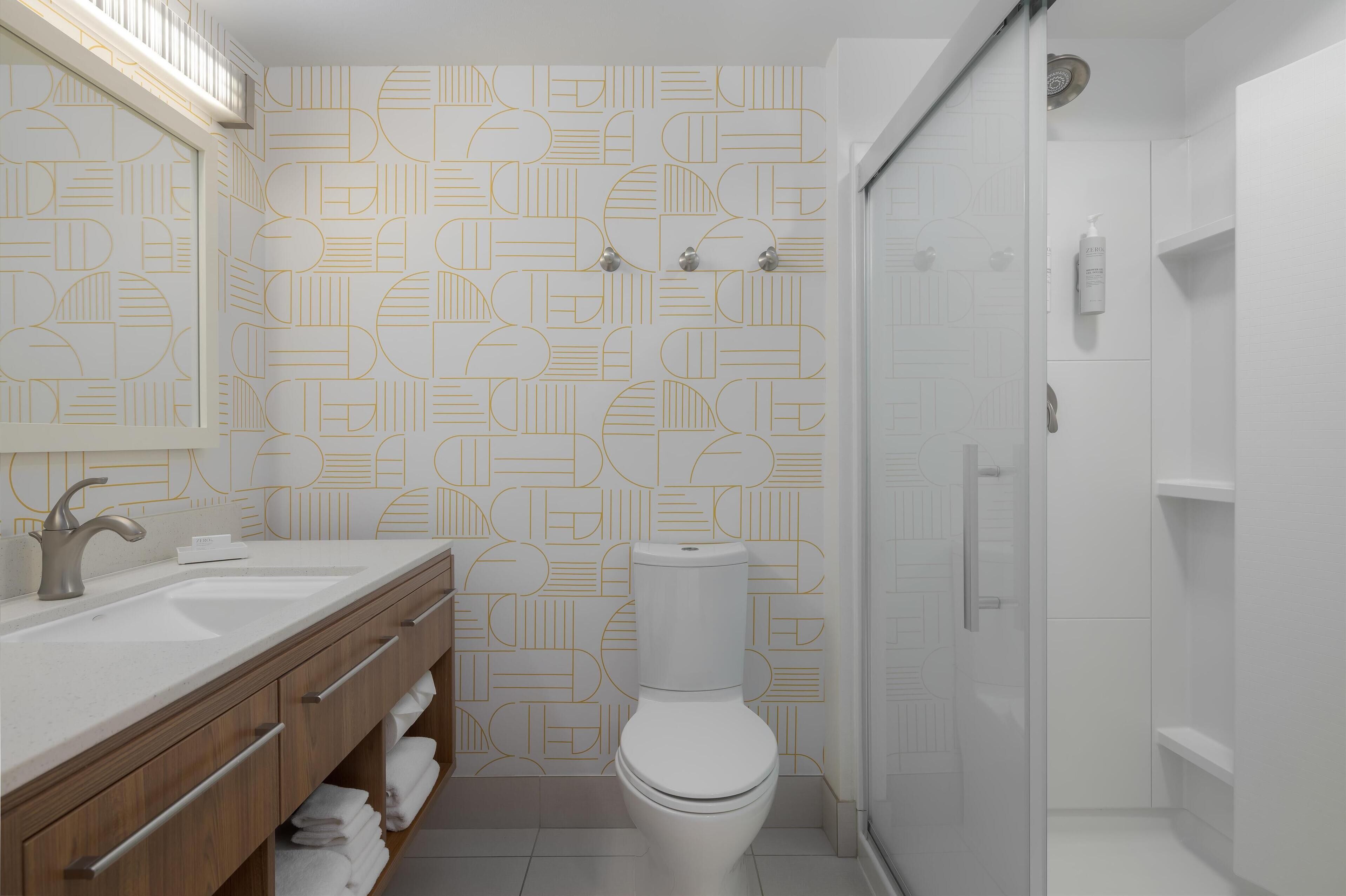 A modern bathroom with a geometric patterned wall, a white toilet, a sink with a faucet, and a shower area.