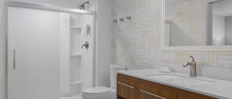 Un baño moderno con cabina de ducha, inodoro y tocador con espejo.