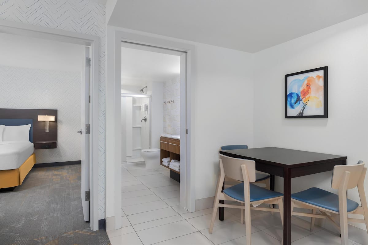 A hotel room with a bed, bedside table, and a bathroom visible through an open door.