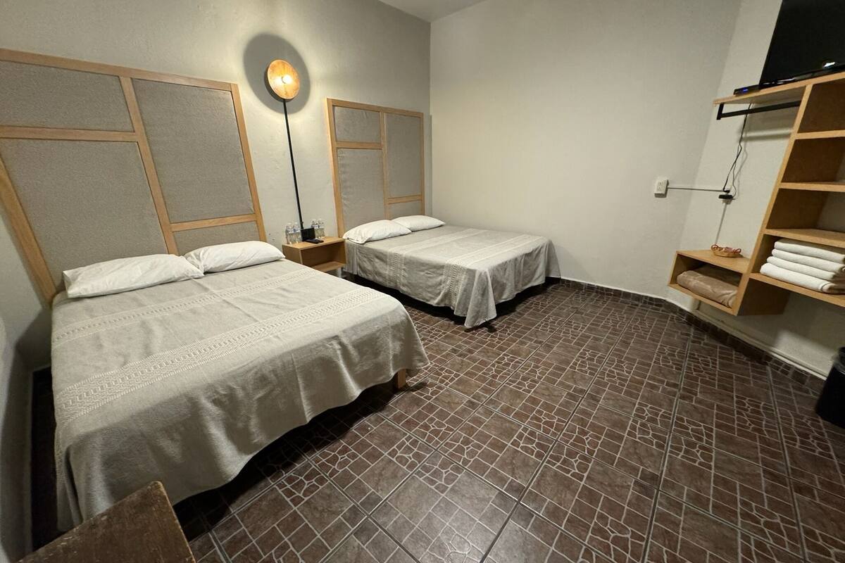Habitación de hotel con dos camas, una lámpara de pie, un televisor en un estante y un perchero.