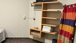A small, neatly organized room with a television on a wooden shelf, a patterned floor, and a striped curtain. - Posada Don Mario (Oaxaca)