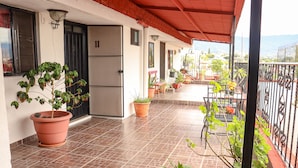 A covered balcony with potted plants, a refrigerator, and a view of the city. - Posada Don Mario (Oaxaca)