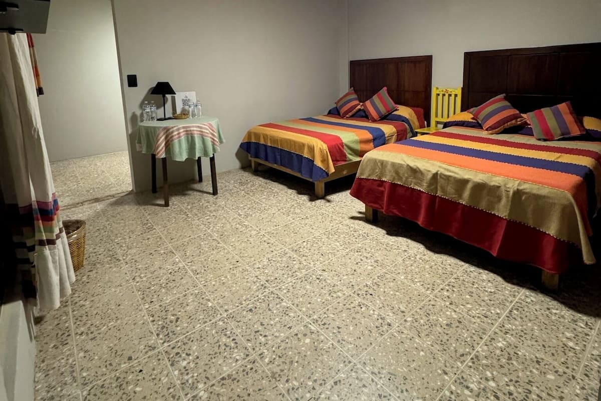 Un dormitorio con dos camas, un ventilador de techo y una mesita de noche con una lámpara.