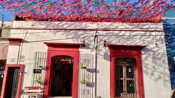 A building with red and white walls, a red door, and a small bench outside. - Posada Don Mario (Oaxaca)