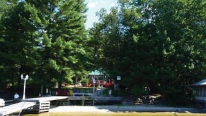A dock with a small boat, surrounded by dense trees and a covered area with seating. - Honey Harbour Cottage (Georgian Bay)