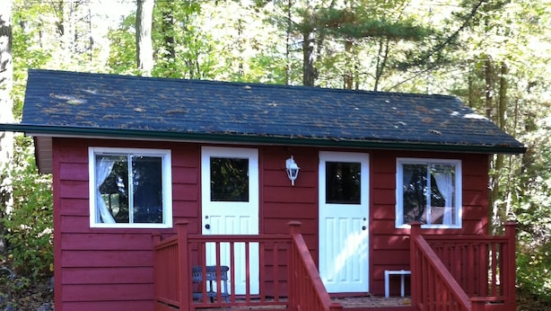 A small, single-story cabin with a red exterior, white trim, and a front porch with a red railing. - Honey Harbour Cottage (Georgian Bay)