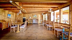 Interior de madera con una mesa de comedor central, sillas, una zona de cocina y ventanas amplias.