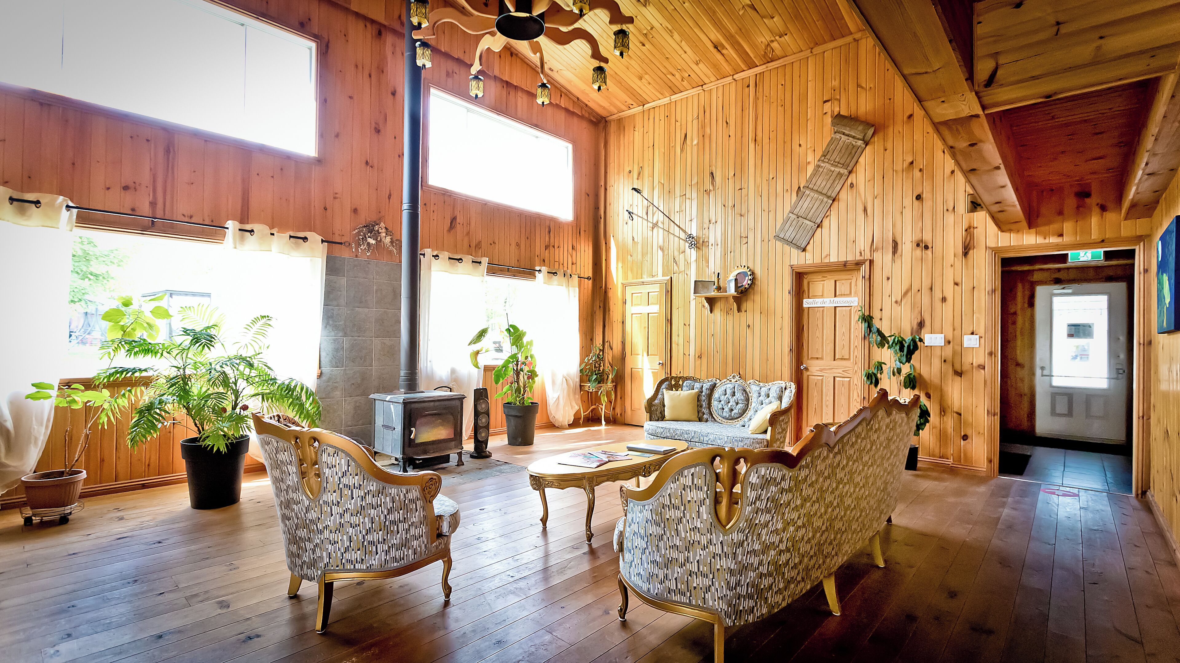 A wooden interior with a fireplace, two ornate chairs, a sofa, and potted plants.