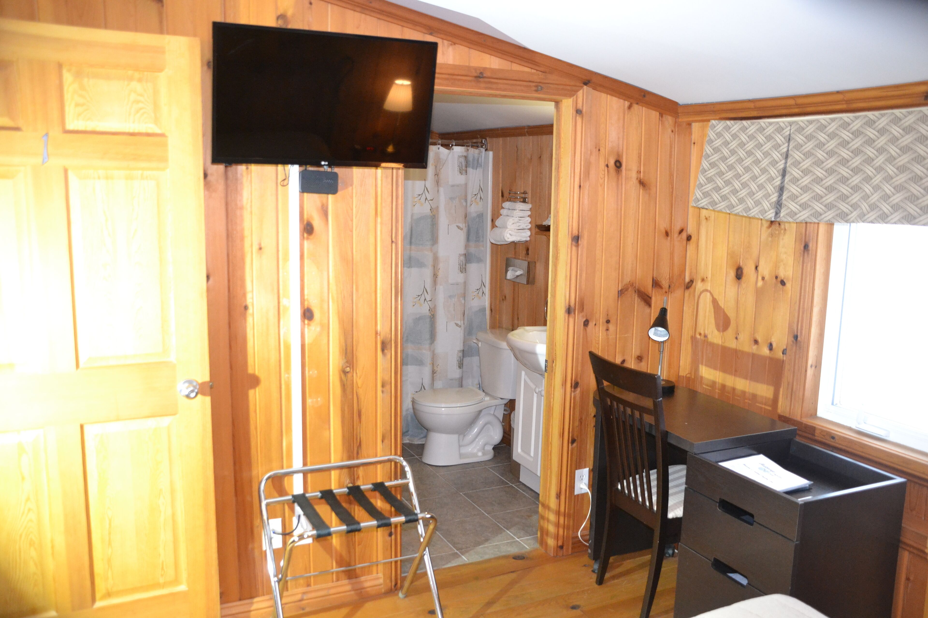 Un intérieur en bois avec un téléviseur fixé au mur, un espace douche, des toilettes et un bureau avec des tiroirs.