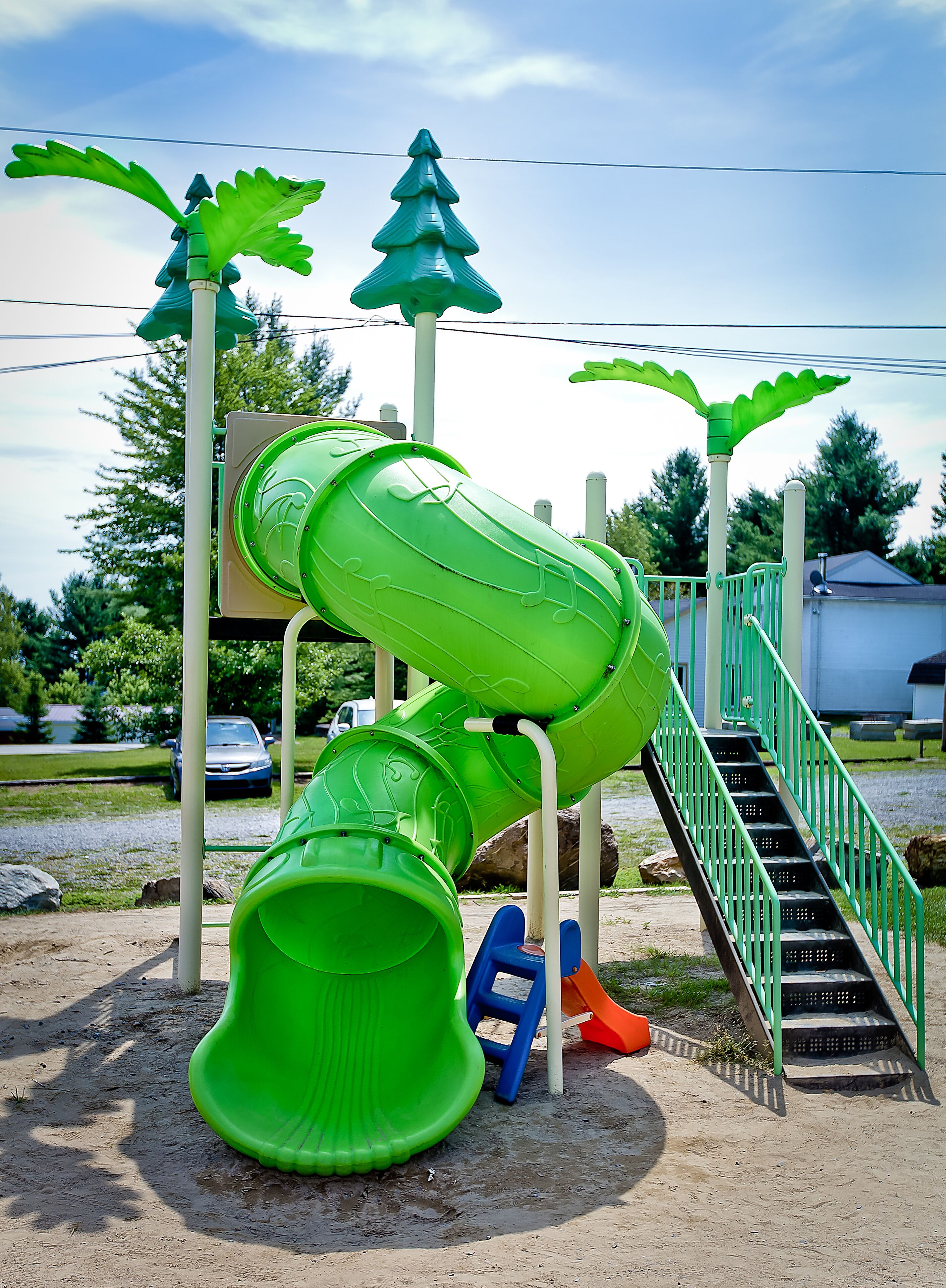 A playground with a green slide, stairs, and decorative elements like palm trees and a Christmas tree.