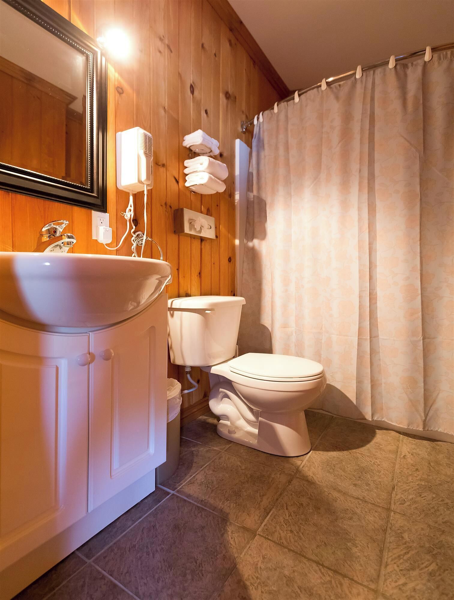 Ein Badezimmer mit Holzwand, Waschbecken in Weiß, Toilette und Duschvorhang.