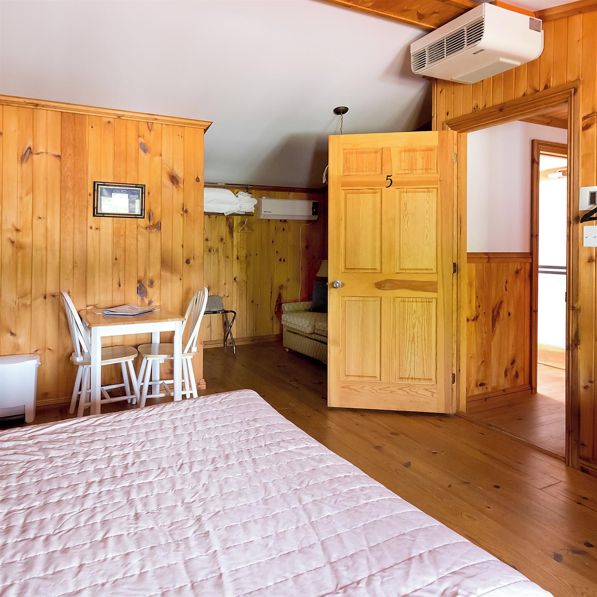 Una habitación de madera con una cama, una mesa y sillas. Se ve una puerta con el número 5.