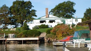 A lakeside property with a dock, a covered boat, and a house with a green roof.