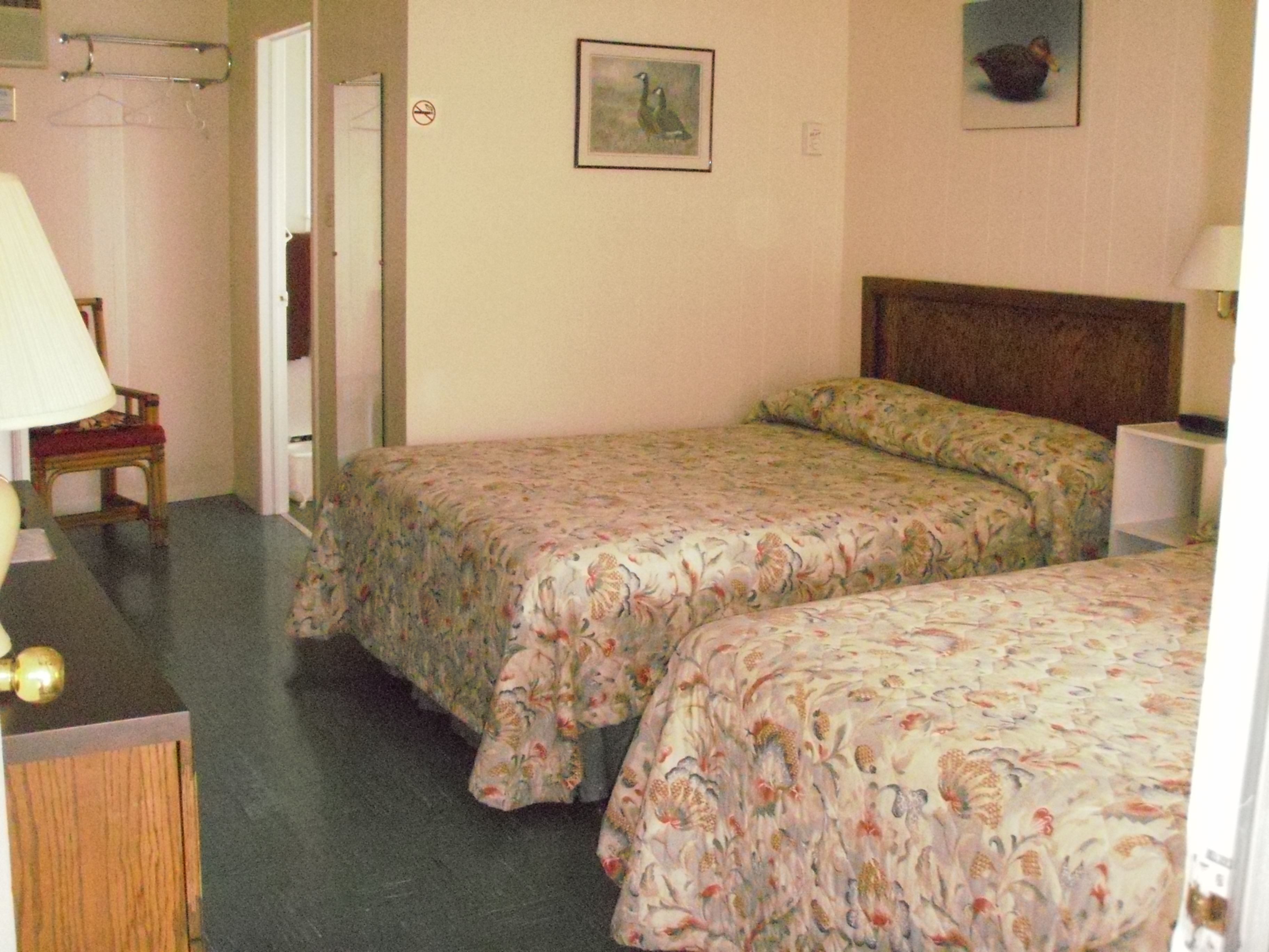 A hotel room with two beds, a chair, a lamp, and a painting on the wall.