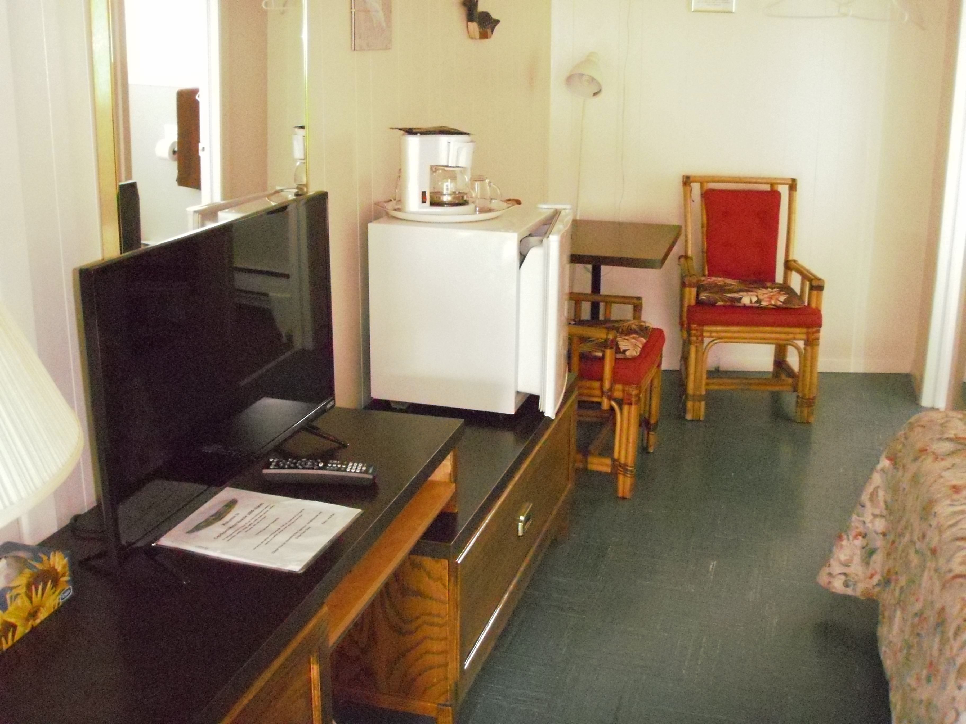 A hotel room with a television, a coffee maker, a refrigerator, a wooden chair, and a bed.