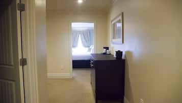 Ein Hotelzimmer mit einem Bett, einem Schreibtisch und einem Stuhl. Ein Fenster mit Vorhängen und eine Tür befinden sich auf der linken Seite.