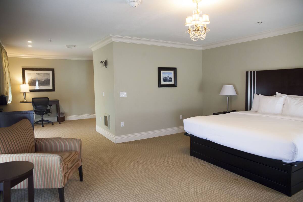 A hotel room with a large bed, a desk with a chair, a small table, and two framed pictures on the wall.