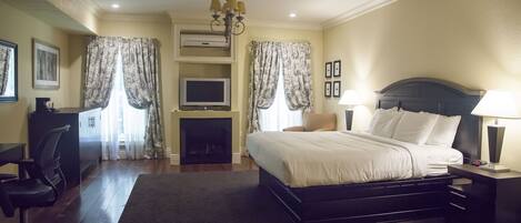 A hotel bedroom with a large bed, a desk, a chair, a TV, and a fireplace.