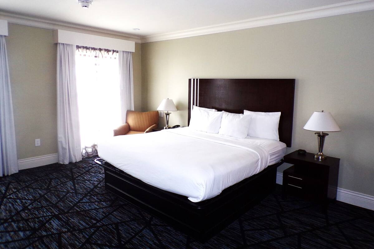 A hotel room with a large bed, two bedside tables with lamps, a chair, and a window with curtains.