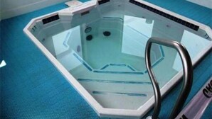 Een rechthoekig whirlpoolbad met een glazen ombouw, een metalen trap en een blauwe vloer.