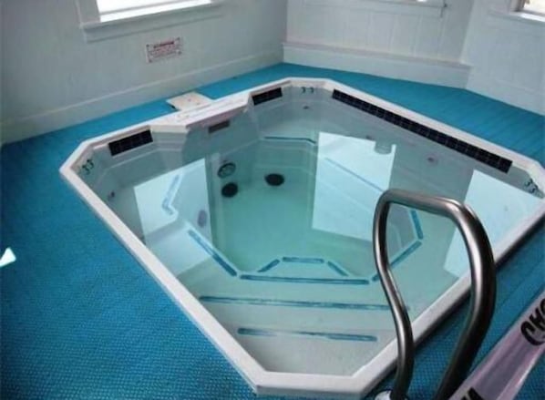 Una bañera de hidromasaje rectangular con cerramiento de vidrio, una escalera metálica y suelo azul.