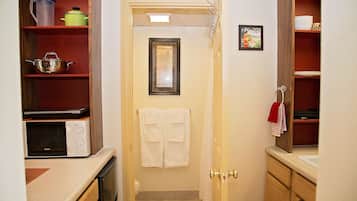 A narrow kitchen with a microwave, stove, and shelves with kitchenware. A door with a towel hanging on it is visible.