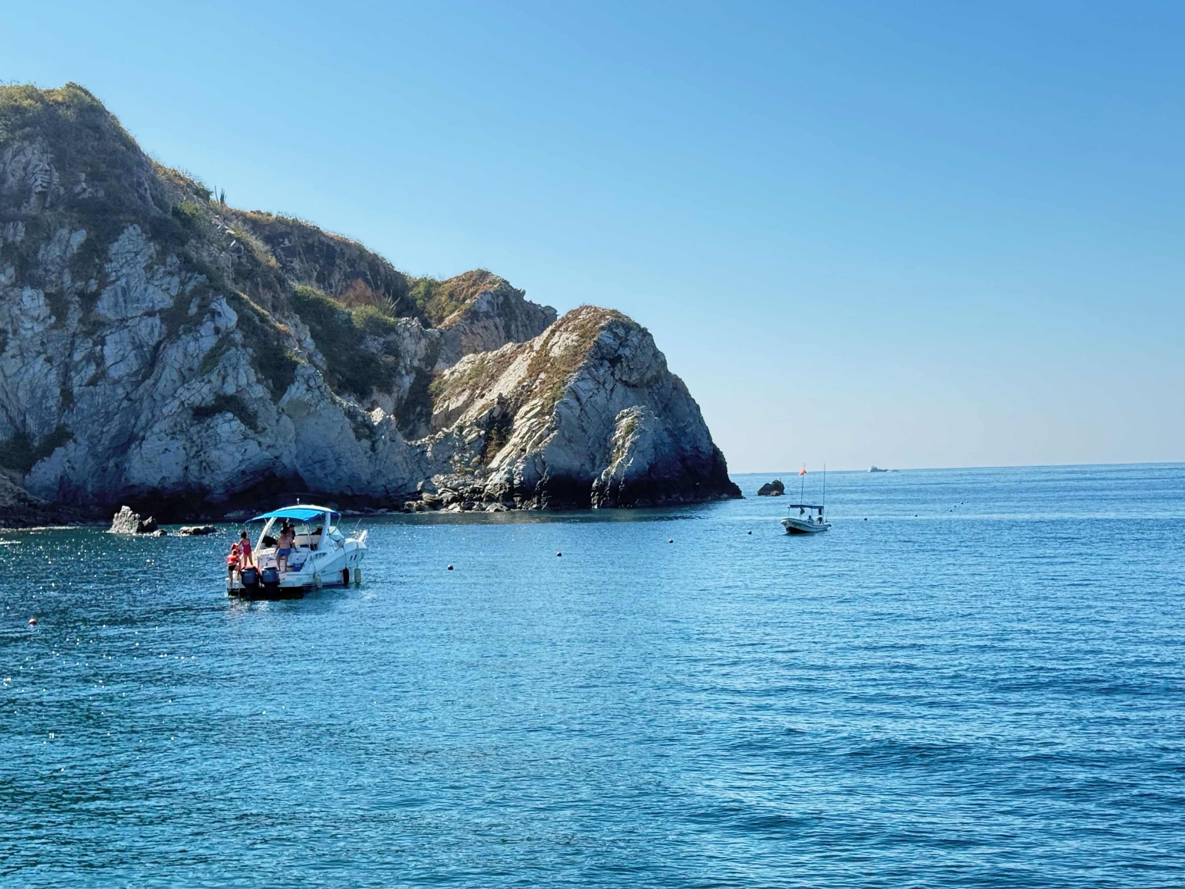 Un barco con pasajeros sobre un mar tranquilo, acantilados rocosos al fondo y un cielo despejado.