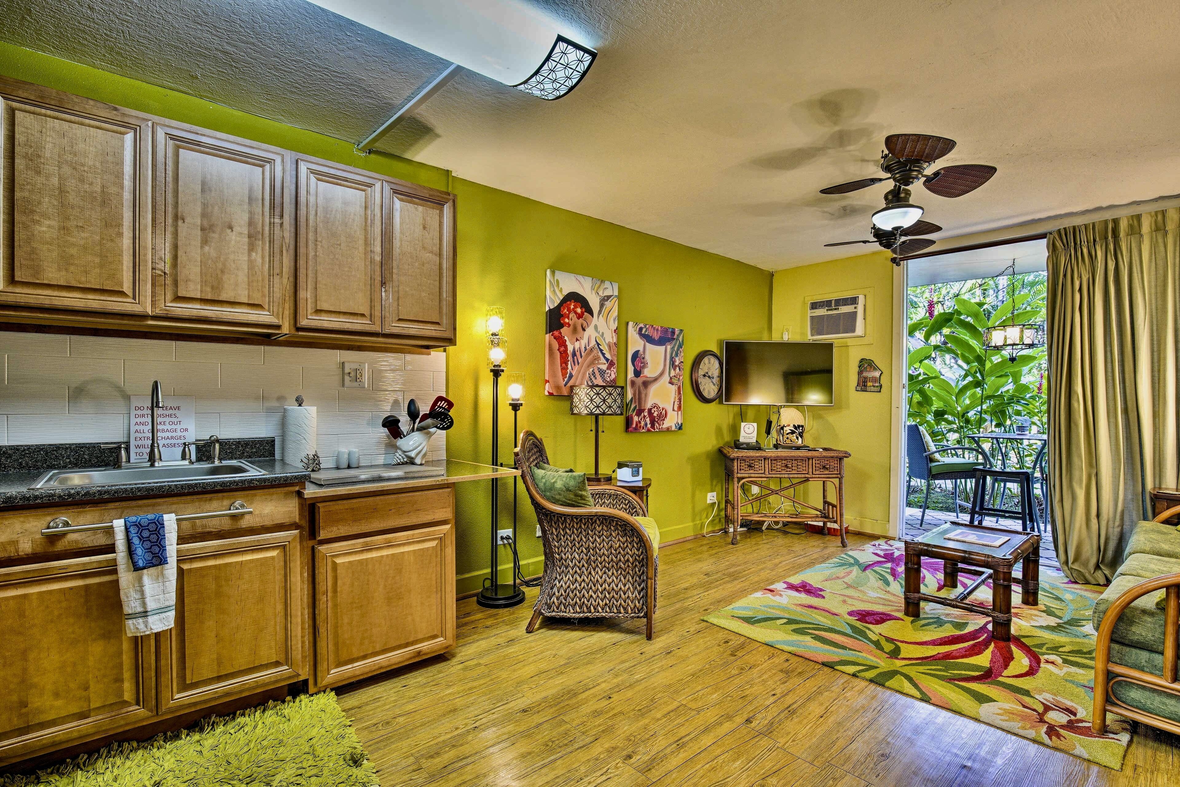 A kitchen with wooden cabinets, a dining area with a chair, a table, and a colorful rug.