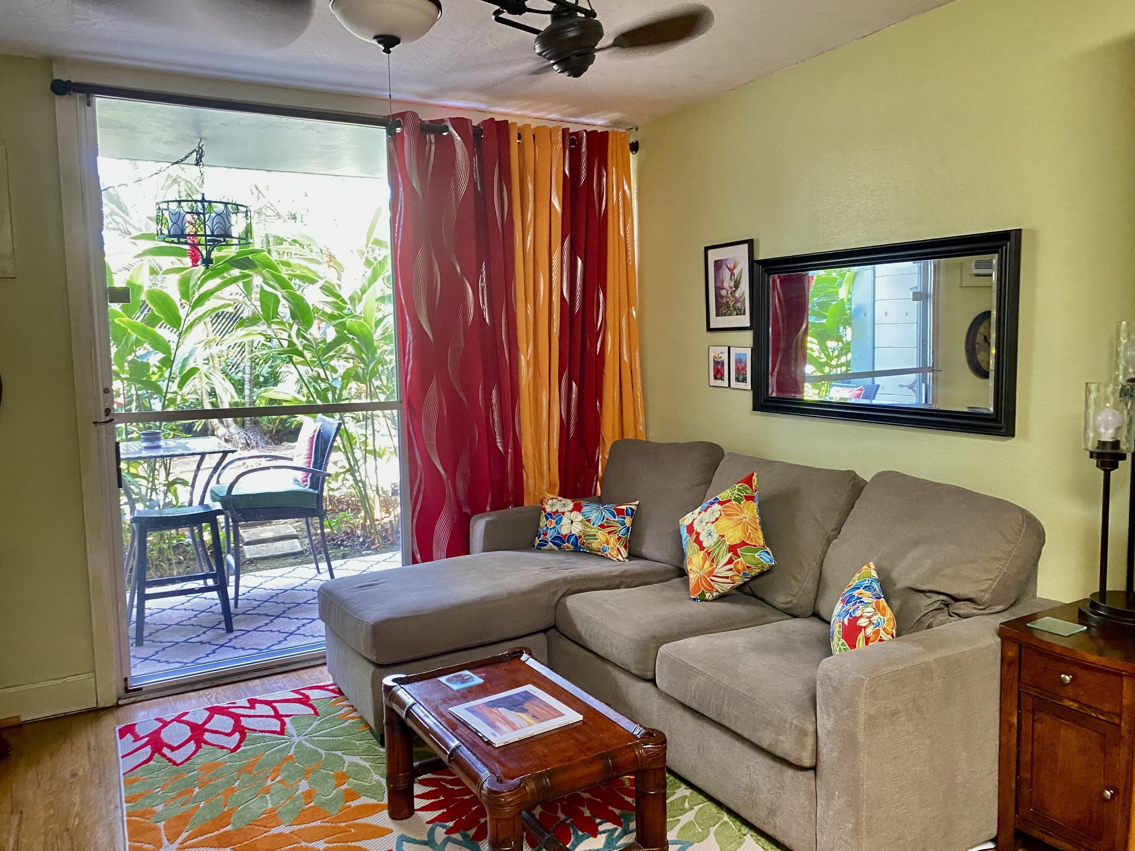 A living room with a sofa, a coffee table, and a view of a balcony with plants.