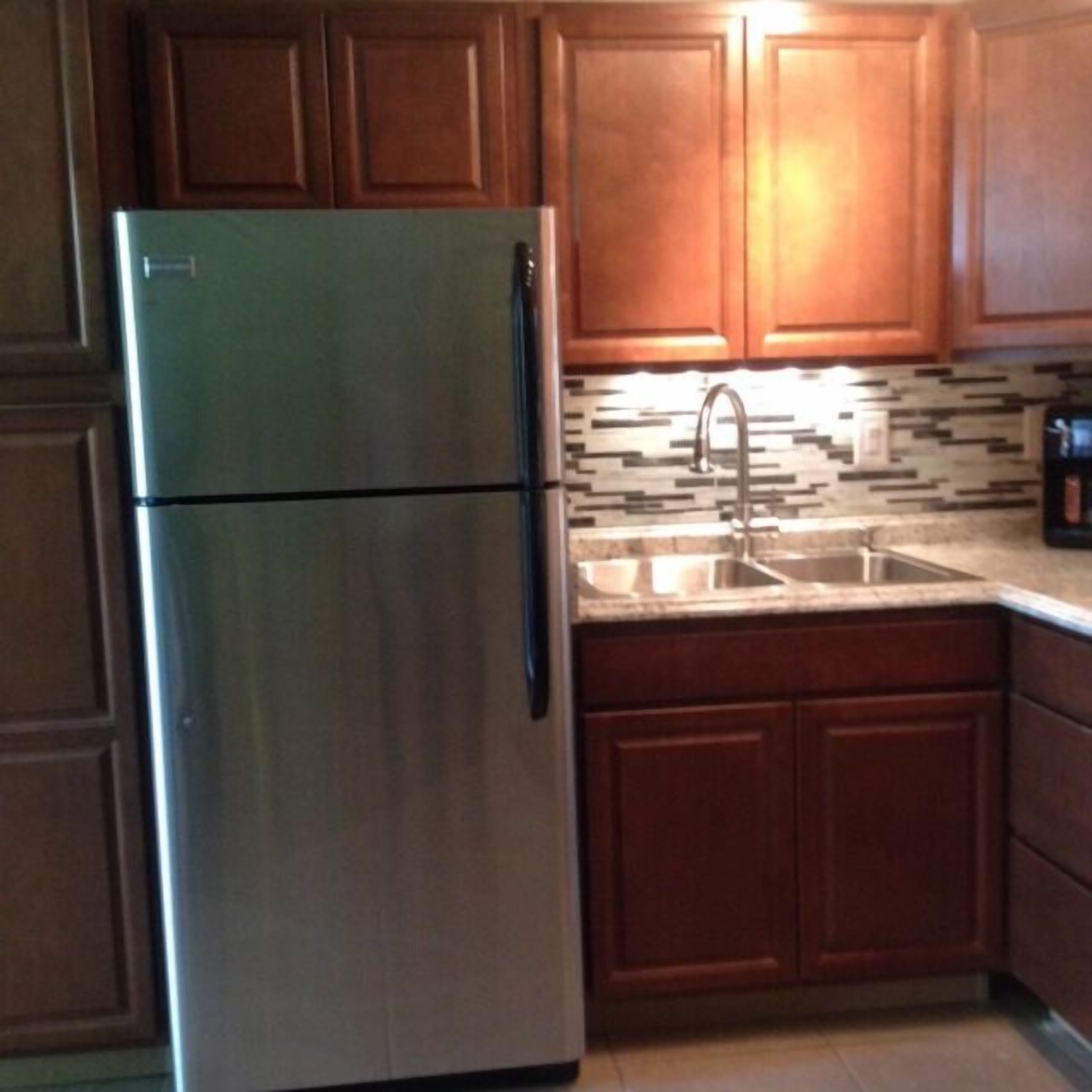 A kitchen with wooden cabinets, a stainless steel refrigerator, a sink, and a tiled backsplash.