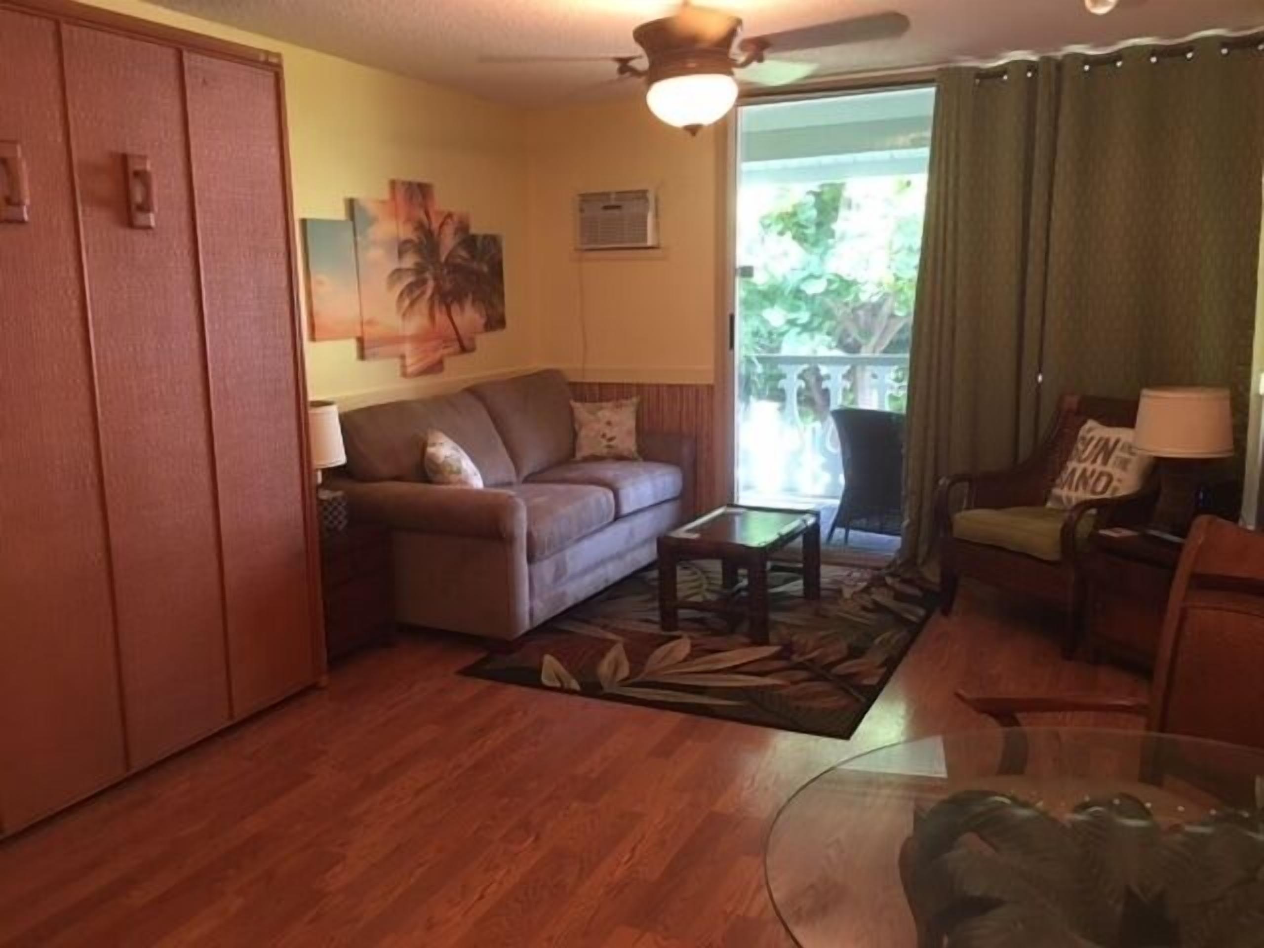 A living room with a sofa, a coffee table, and a chair. There is a sliding glass door leading to an outdoor area.