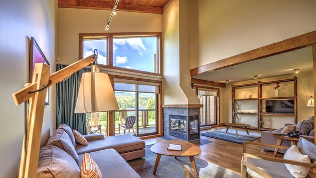 A spacious living room with a fireplace, comfortable seating, and large windows offering a view of the outdoors. - Le Grand R (Saint Donat)