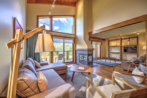 A spacious living room with a fireplace, comfortable seating, and large windows offering a view of the outdoors. - Le Grand R (Saint Donat)