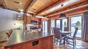 A modern kitchen with a central island, wooden cabinets, stainless steel appliances, and a view of a snowy landscape through large windows. - Le Grand R (Saint Donat)